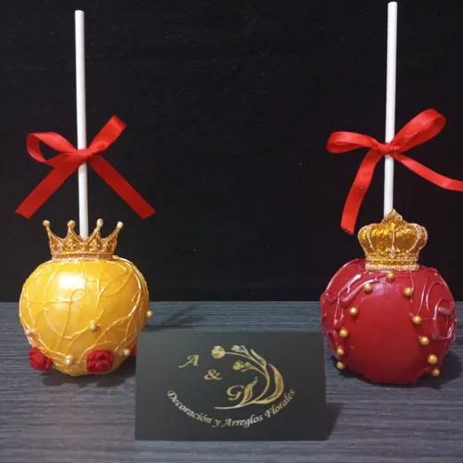 Dos manzanas decoradas, una dorada y una roja, con corona y moño rojo